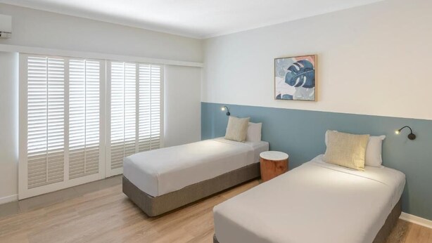 A bedroom with two beds, a window with blinds, a wall-mounted artwork, and a ceiling fan. - Ramada Resort Port Douglas (2 Bedroom Apartment) (Port Douglas)
