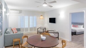 A modern living room with a round wooden table, a grey sofa, and a television mounted on the wall. - Ramada Resort Port Douglas (2 Bedroom Apartment) (Port Douglas)