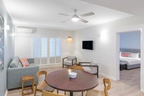 Ein modernes Wohnzimmer mit einem runden Holztisch, einem grauen Sofa und einem an der Wand befestigten Fernseher.