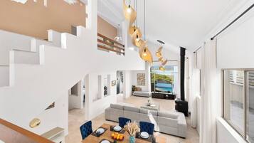 A modern interior with a dining area, a sofa set, and a staircase.