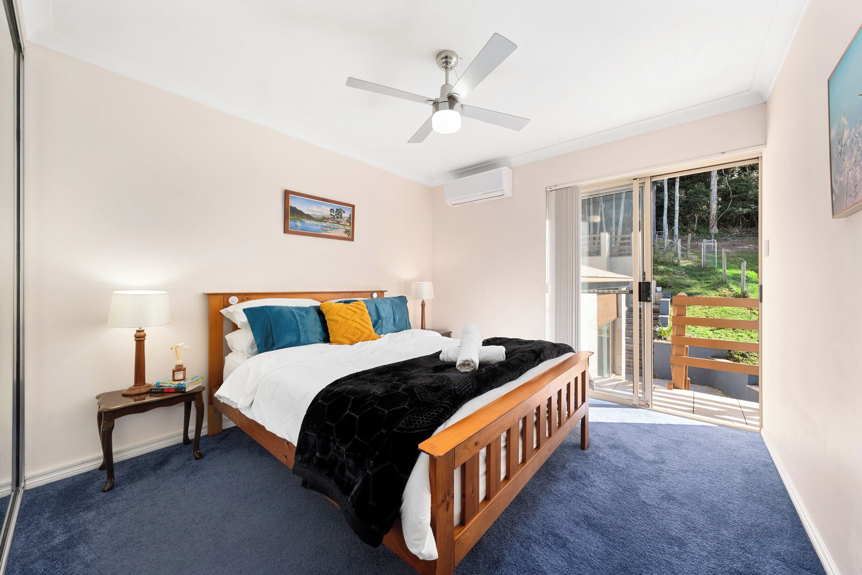 A bedroom with a bed, a nightstand, a lamp, a ceiling fan, and a view of the outdoors.