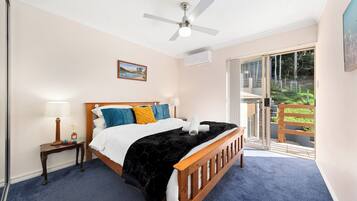 A bedroom with a bed, a nightstand, a lamp, a ceiling fan, and a view of the outdoors.