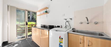 Una cocina moderna con lavadora incorporada, un lavamanos y una puerta corrediza de vidrio que da a un balcón.