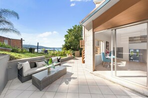 A modern outdoor patio with a seating area, a glass door leading to a room, and a view of the sea.