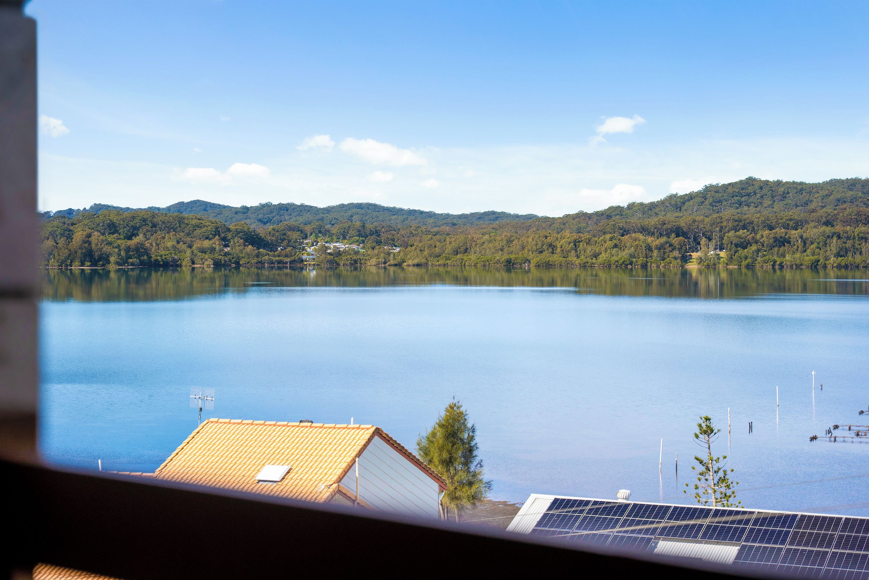 A lake with a view of a building with a tiled roof and solar panels in the foreground.