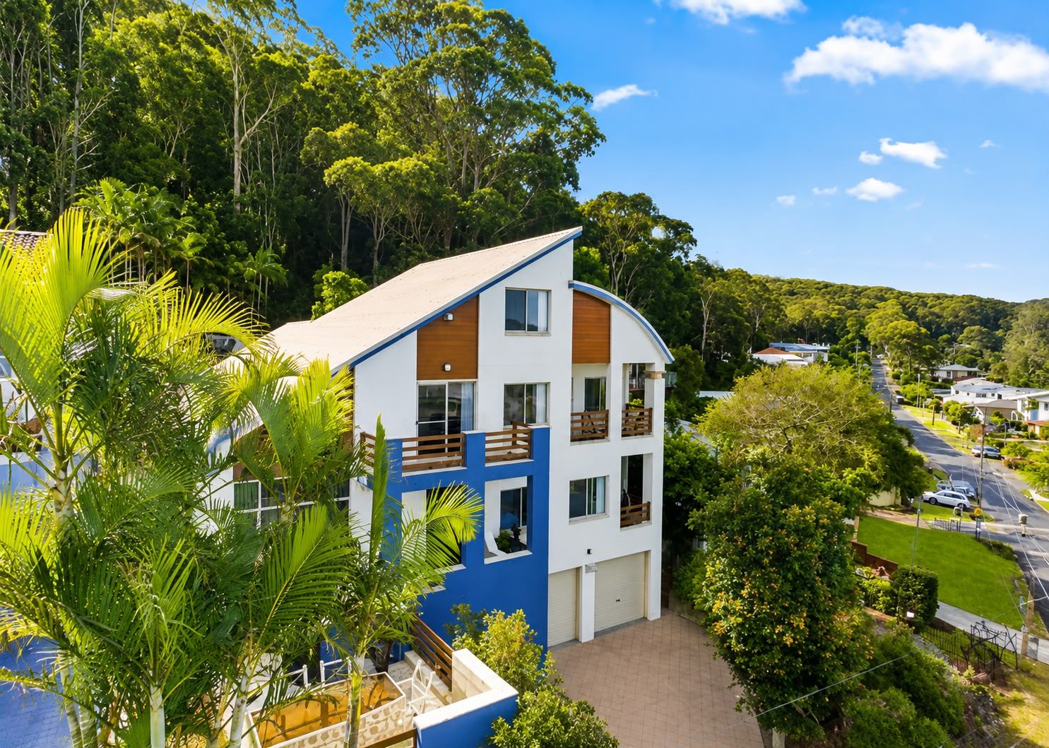 A multi-story building with balconies, surrounded by lush greenery and a clear sky.