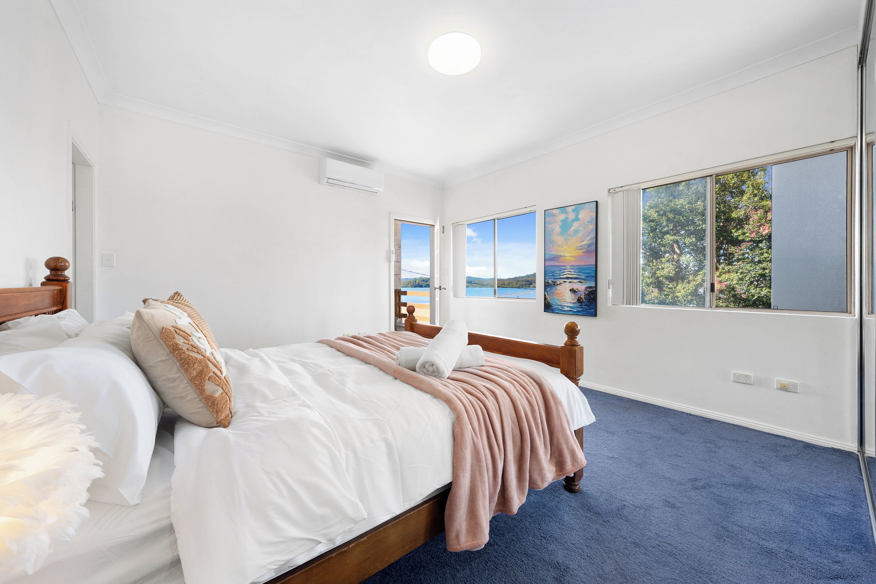 A bedroom with a large bed, a window with a view of a landscape, and a painting on the wall.