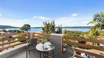 A balcony with a table and chairs, overlooking a body of water and greenery.