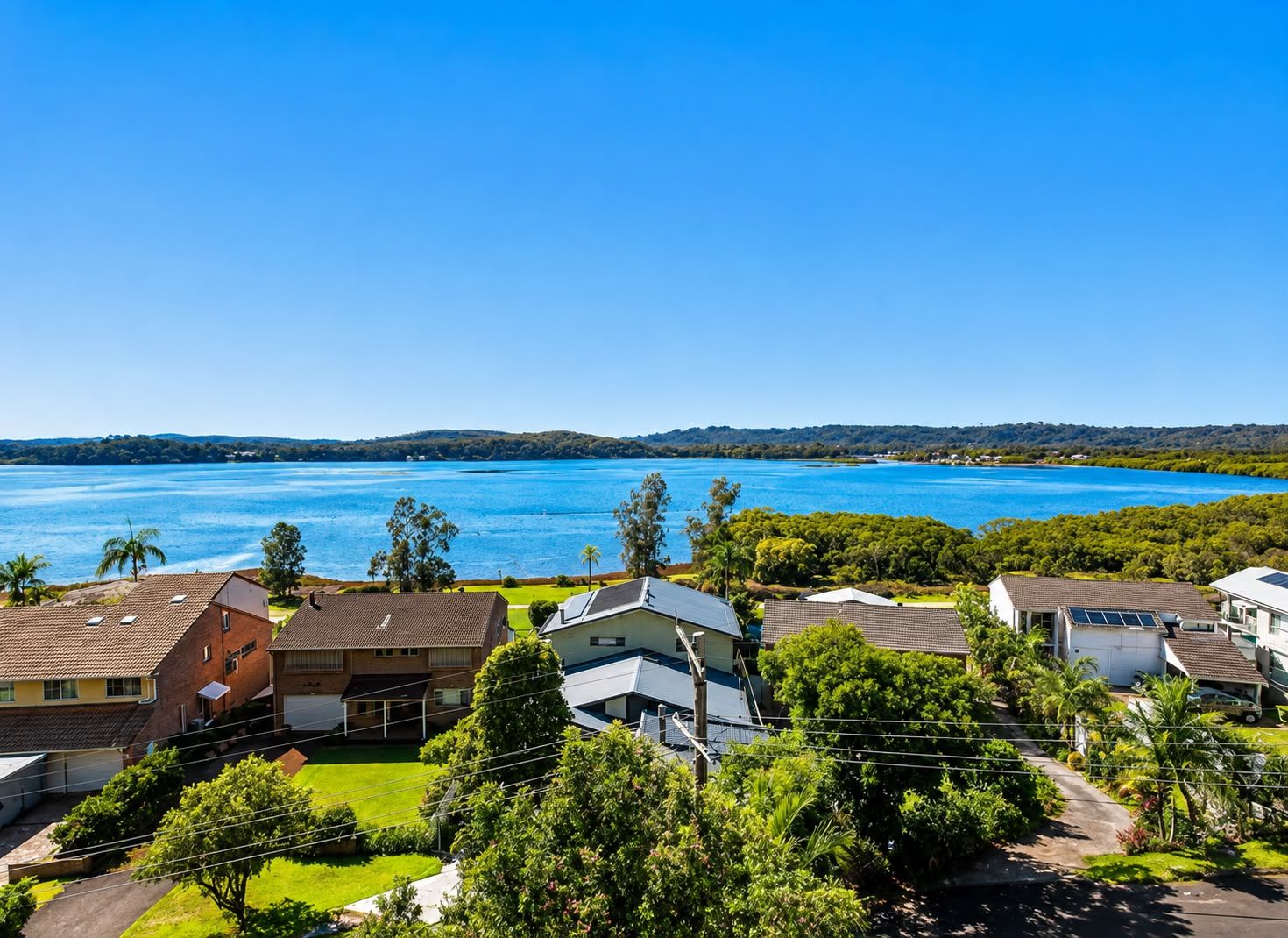 A residential area with houses, a clear blue sky, and a large body of water in the background.