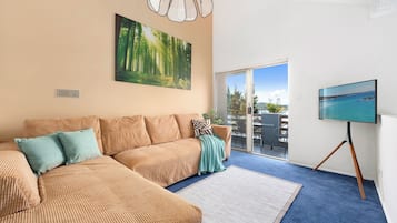 Uma sala de estar moderna com um sofá modular, uma TV de tela plana e uma grande janela com vista para o exterior.