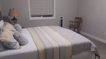 A bedroom with a bed, a nightstand, a lamp, a chair, and a window.