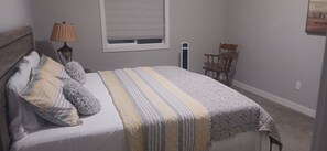 A bedroom with a bed, a nightstand, a lamp, a chair, and a window.