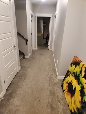 A hallway with carpeted flooring, white walls, and a door on the left.