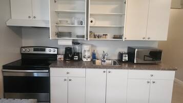 Una cucina compatta con mobili bianchi, un fornello, un forno a microonde e una macchina per caffè.