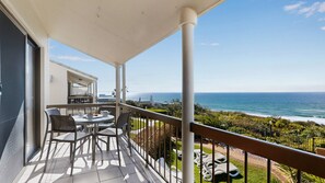 Een balkon met uitzicht op de oceaan, buitenmeubilair en een gebouw op de achtergrond.