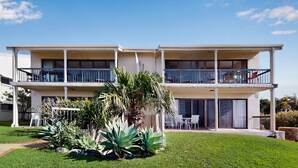 Ein zweistöckiges Wohngebäude mit Balkon an jeder Etage, einem gepflegten Rasen und verschiedenen Pflanzen.