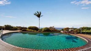 Ein klarer Pool mit Ziegelrand, umgeben von viel Grün und Blick aufs Meer.