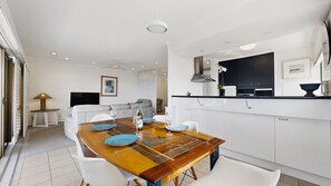 Een moderne keuken met witte kasten, een zwart aanrecht en een eethoek met een houten tafel en witte stoelen.