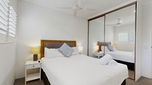 Een hotelkamer met een bed, nachtkastjes, een spiegel en een plafondventilator.