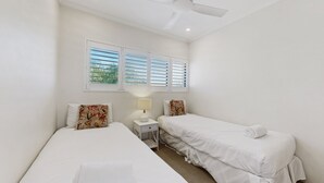 Ein Zimmer mit zwei Betten, einem Nachttisch, einer Lampe und einem Deckenventilator.