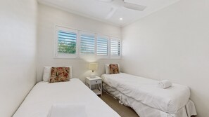 Ein Zimmer mit zwei Betten, einem Nachttisch, einer Lampe und einem Deckenventilator.