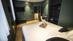 Quarto de hotel com cama, escrivaninha, cadeira, guarda-roupa e televisão.