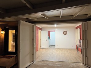 An interior hallway with a wooden floor, white walls, and a red accent wall. There is a white door at the end of the hallway, and a clock on the wall. - The Bar House (Seligman)
