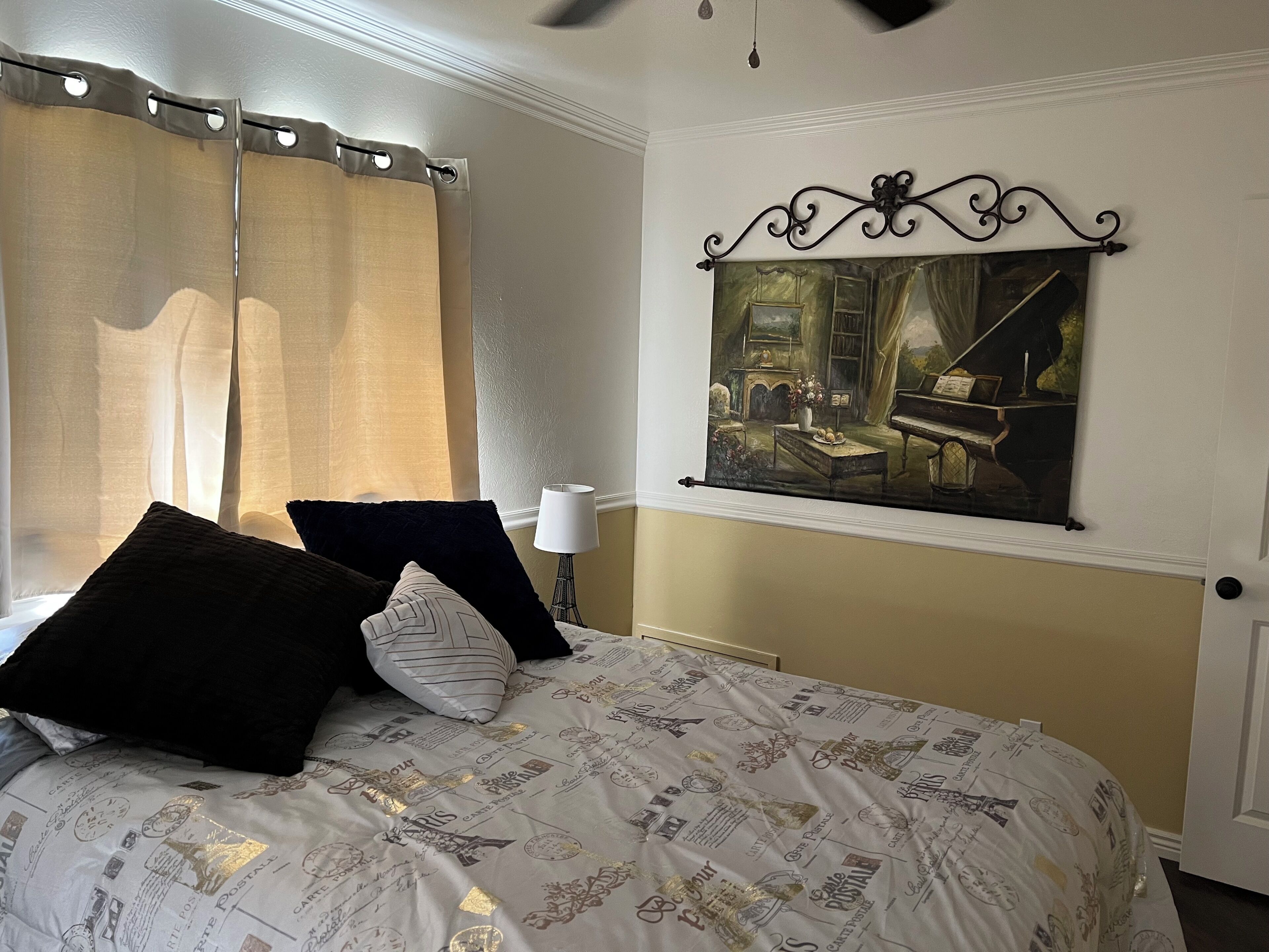 Un dormitorio con cama, cortinas, un cuadro y una lámpara.
