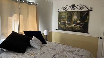 Un dormitorio con cama, cortinas, un cuadro y una lámpara.