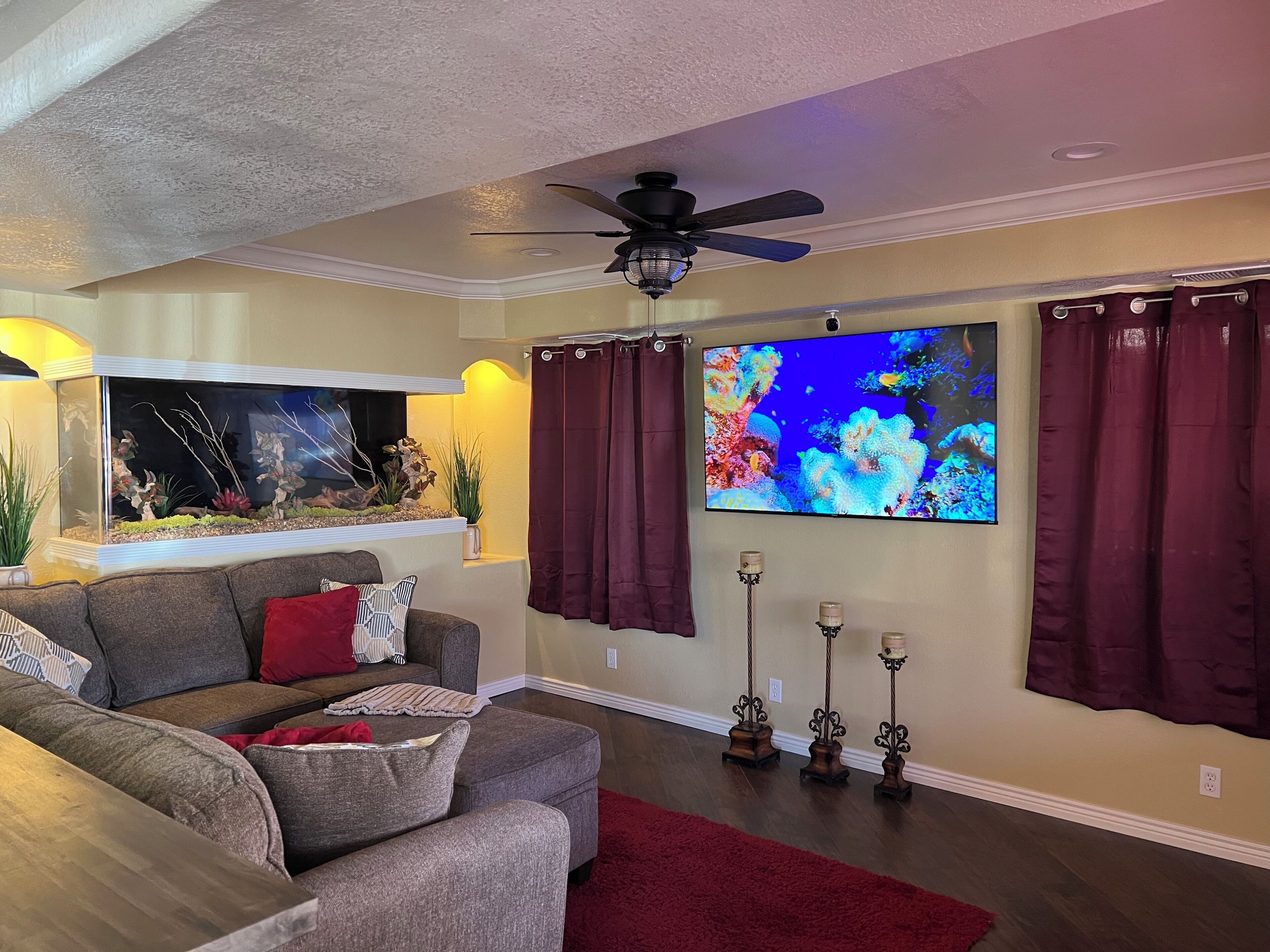 A living room with a gray sofa, a fish tank, a flat-screen TV, and a ceiling fan.