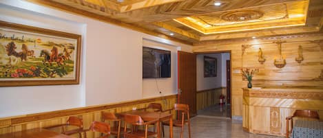 A hotel lobby with wooden paneling, a reception desk, and a dining area with chairs and tables.