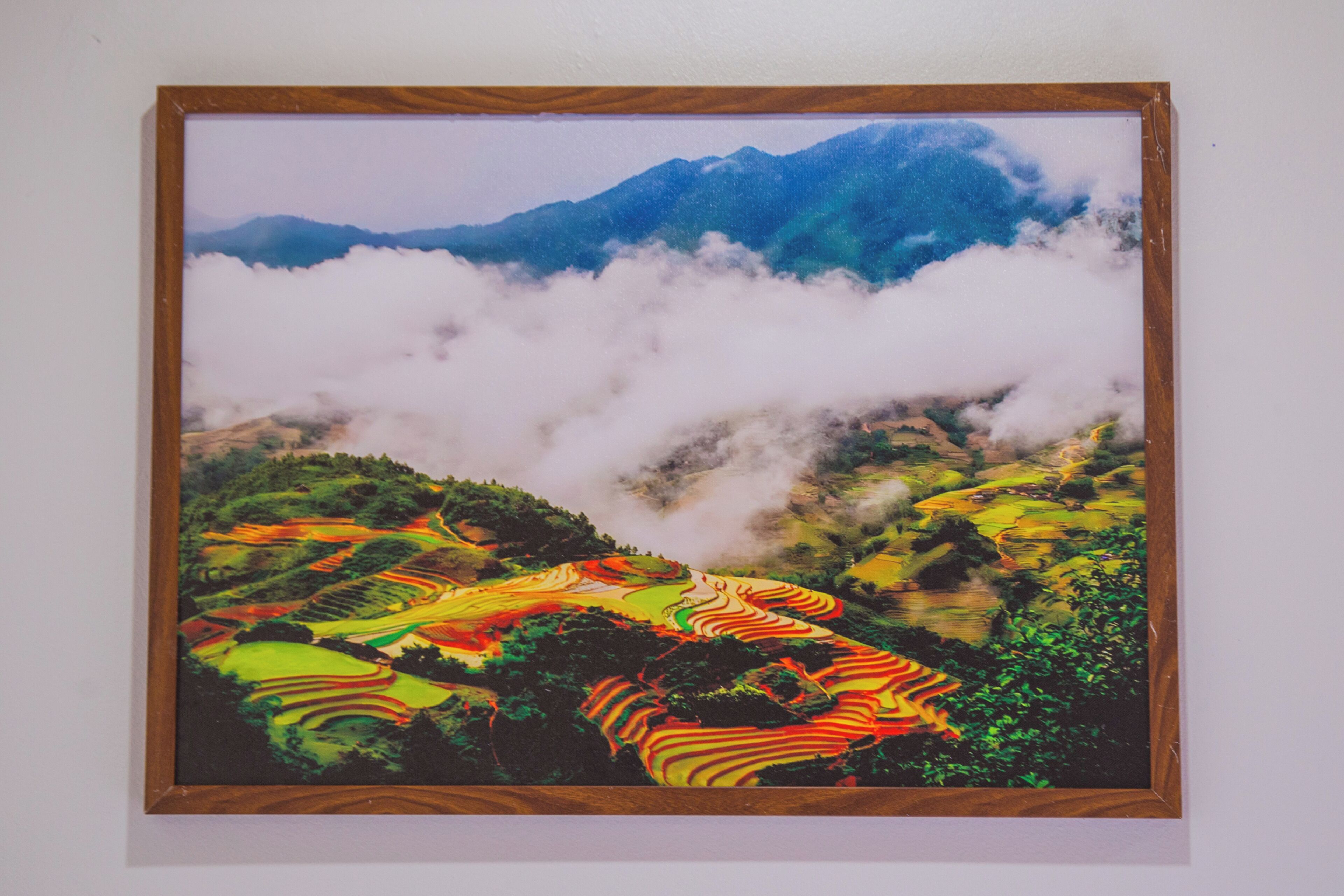 Una pintura de paisaje enmarco, con montañas y nubes al fondo.