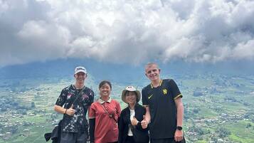 Um grupo de pessoas está em uma colina gramada, apreciando a vista panorâmica de um vale e montanhas ao fundo.