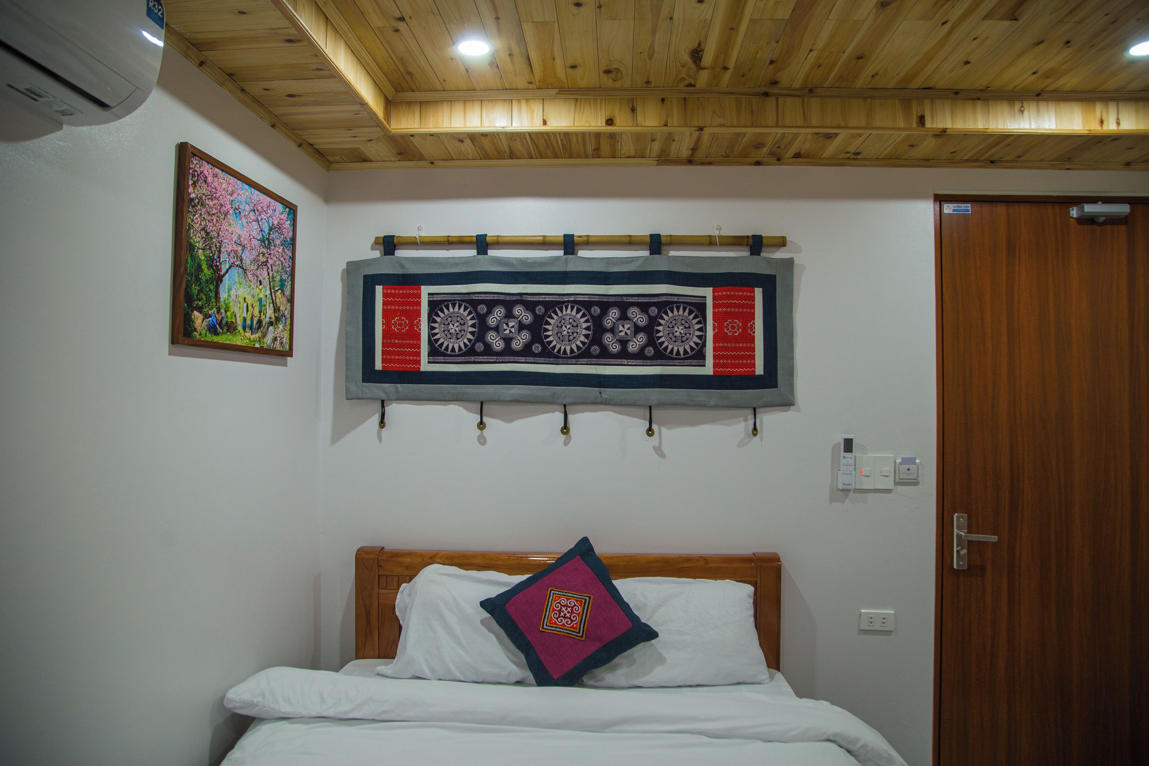 A bedroom with a wooden ceiling, a bed with white bedding, a decorative tapestry, and a painting on the wall.