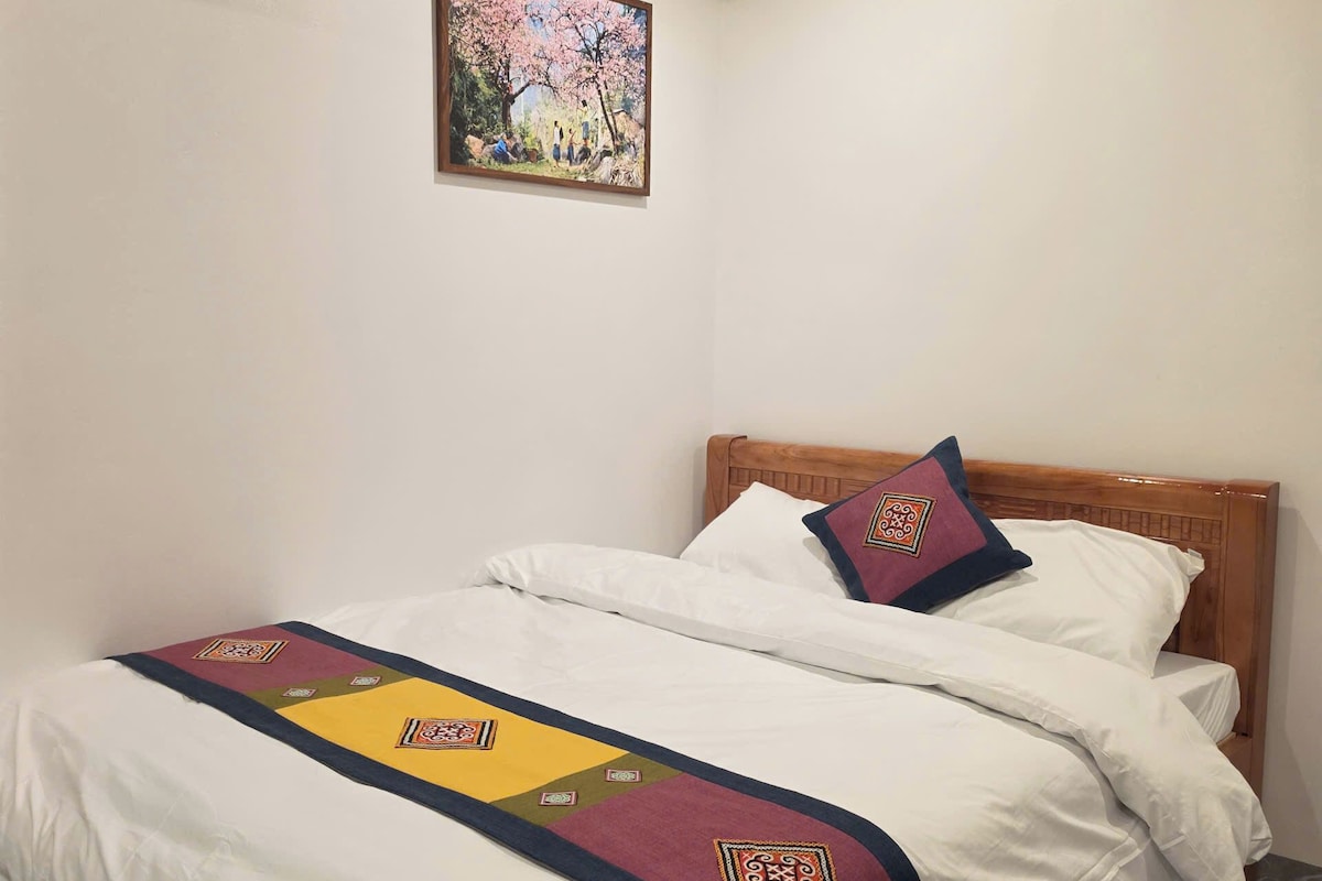A bedroom with a wooden ceiling, a bed with white bedding and decorative pillows, a painting on the wall, and an air conditioning unit.