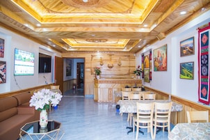 Un hall de hotel con techo de madera, una recepción, un área de descanso con mesas y sillas, y obras de arte en las paredes.