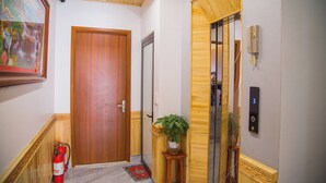 Passatge amb una porta de fusta, un extintor, una planta en test i un telèfon penjat a la paret.