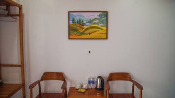 Ein Zimmer mit zwei Holzstühlen, einem kleinen Tisch mit Tassen, einem Wasserkocher und einem Landschaftsbild an der Wand.