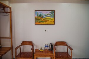 A room with two wooden chairs, a small table with cups, a kettle, and a painting of a landscape on the wall.