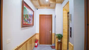 Un pasillo con una puerta de madera, un extintor, un teléfono y un cuadro en la pared.
