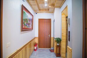 Un pasillo con una puerta de madera, un extintor, un teléfono y un cuadro en la pared.