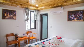 Una habitación de hotel con techo de madera, una cama con cubrecama blanco y decoraciones con forma de corazón, un escritorio de madera con sillas y dos cuadros en las paredes.
