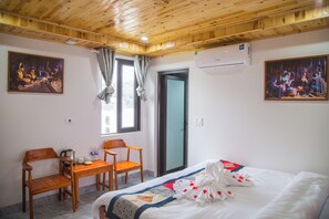 Una habitación de hotel con techo de madera, una cama con cubrecama blanco y decoraciones con forma de corazón, un escritorio de madera con sillas y dos cuadros en las paredes.