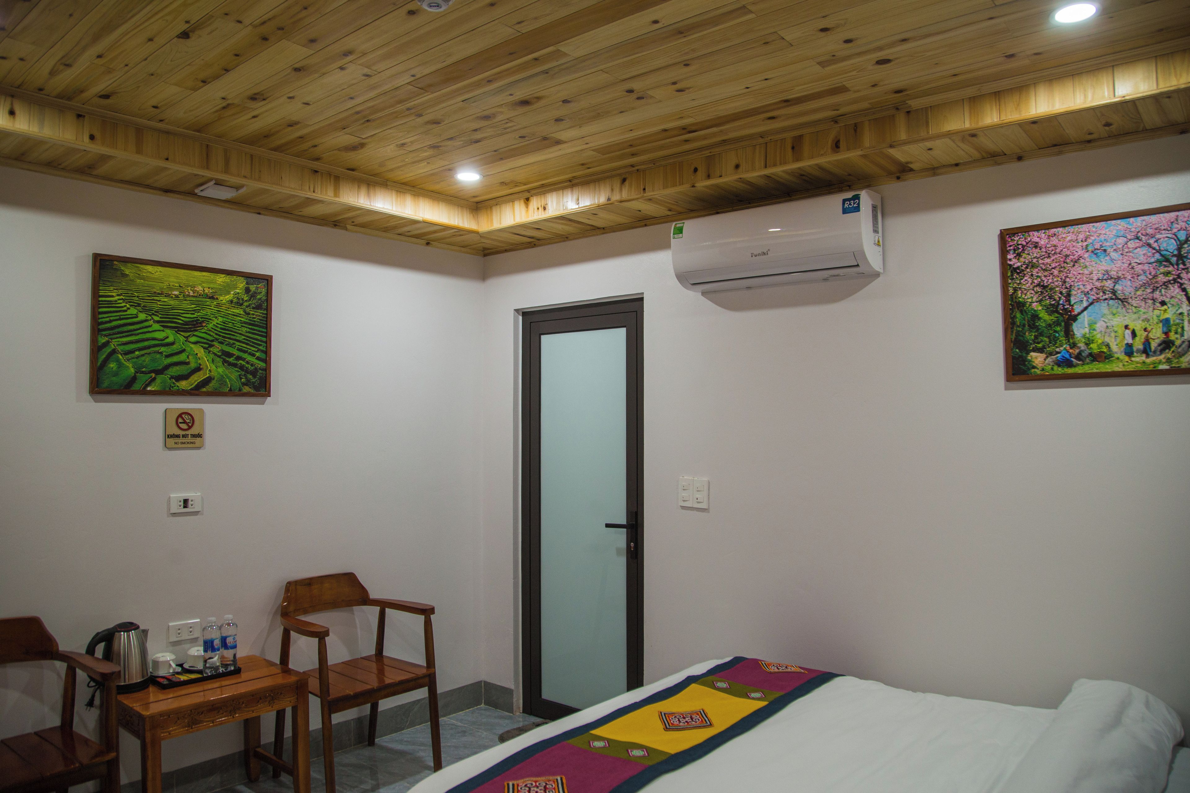 Een hotelkamer met een houten plafond, een bed met een kleurrijke deken, een bureau met stoel en een schilderij aan de muur.