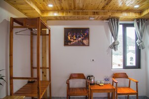 Una habitación con techo de madera, un cuadro de personas, una ventana con cortinas y dos sillas de madera.
