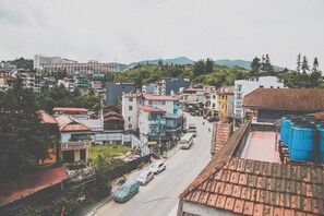 A street view of a town with buildings, vehicles, and a hilly landscape in the background.