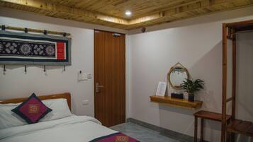 Ein Zimmer mit einem Bett, einer Holztür, einem an der Wand befestigten Spiegel und einem Regal mit einer Pflanze.