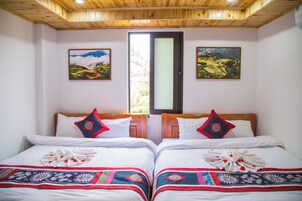 A double room with two beds, each with a white bedspread and decorative pillows. There are two framed landscape paintings on the walls.