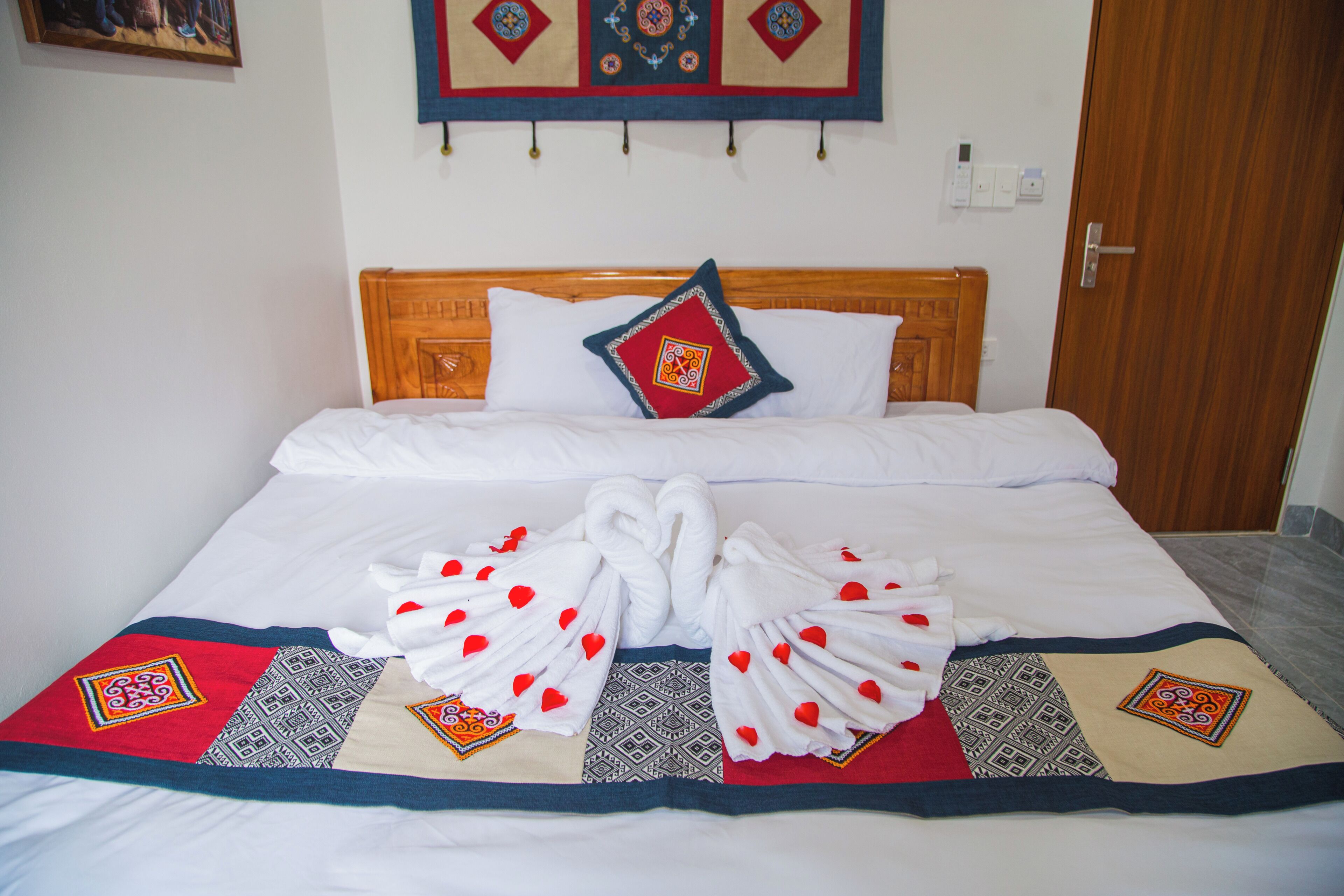 Una cama bien tendida con un cabecero decorativo, un colcha con diseños geométricos y un arreglo de toallas sobre la colcha.