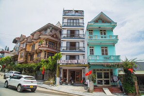 Un hotel con un cartel que dice 'SAPA STATION HOTEL' frente a un edificio de varios pisos con balcones y vista a la calle.